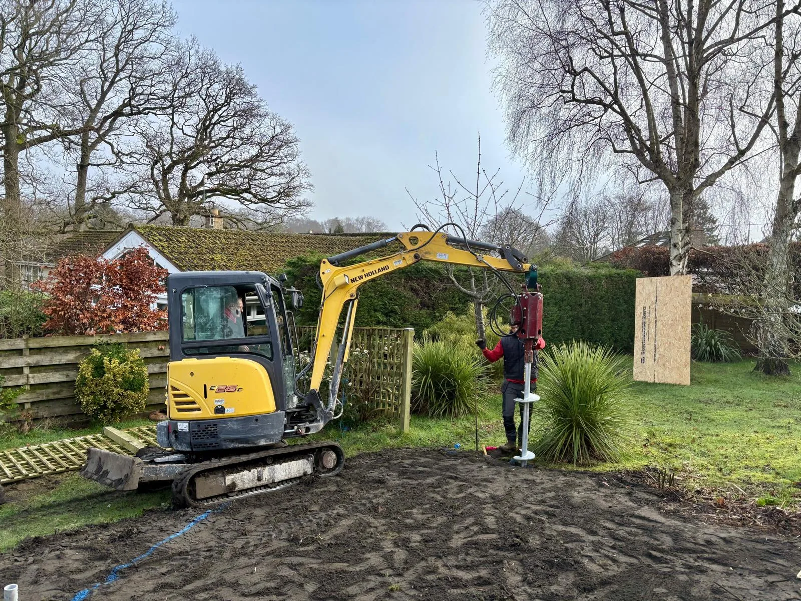 Excavator installing screw pile foundations on a garden site